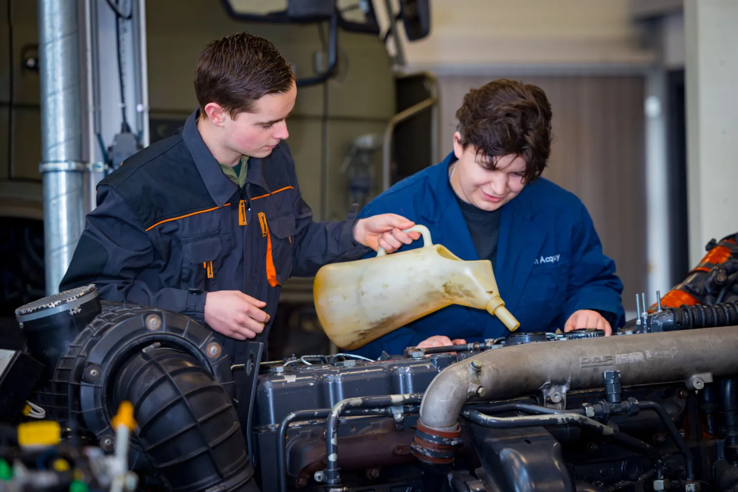 De olie van een vrachtwagen wordt gecontroleerd en bijgevuld door twee studenten bedrijfsautotechniek