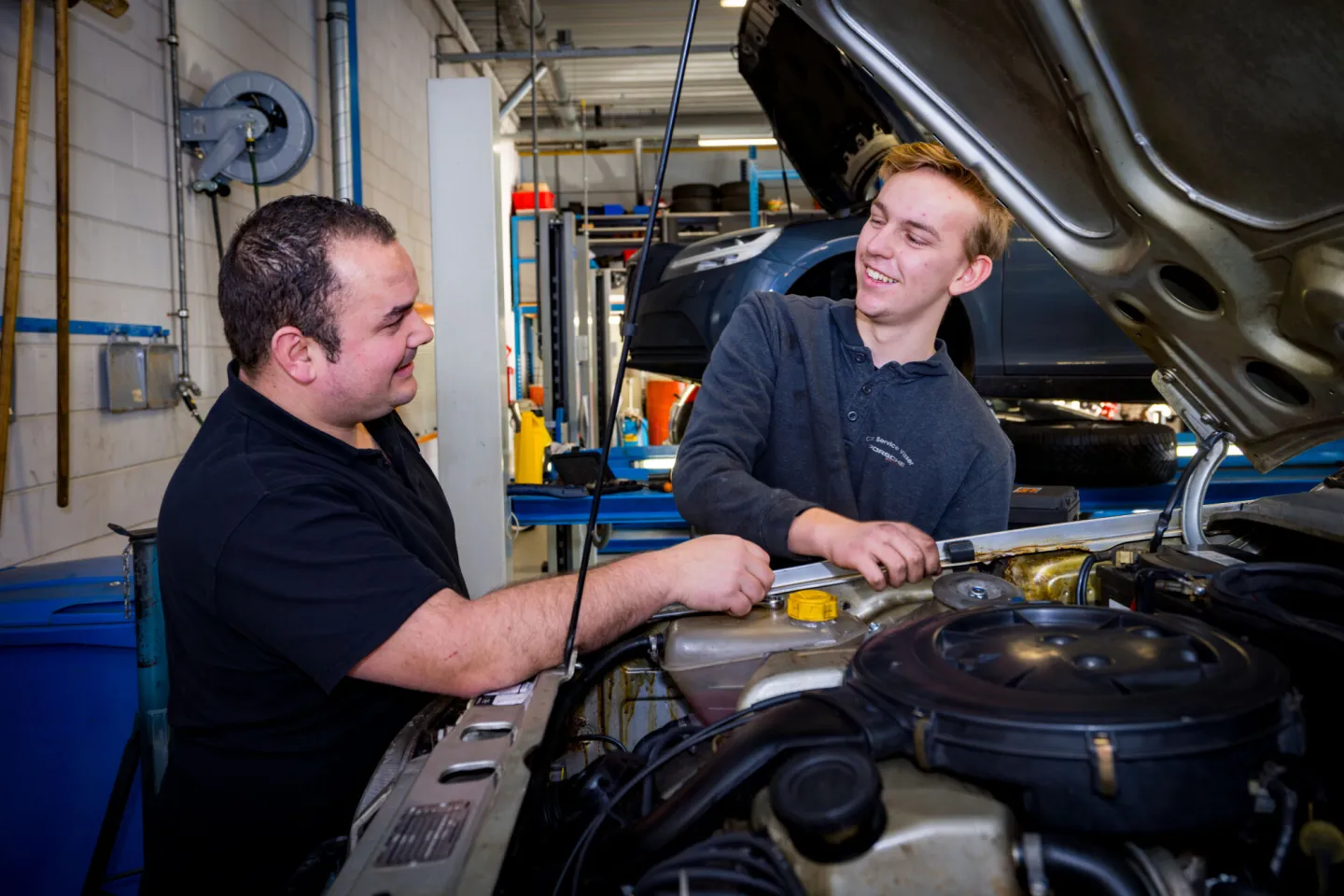 Twee monteurs sleutelen aan een auto in een garage.