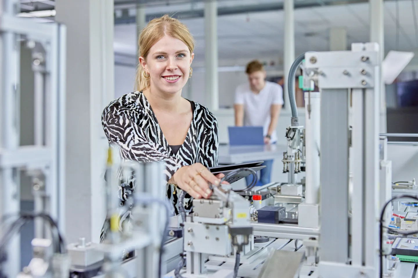 Een jonge dame staat bij een machine met een laptop in haar hand en is bezig met het instellen ervan. 