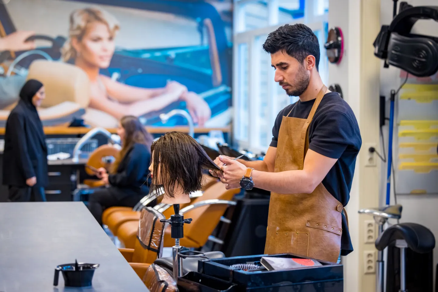 Een man met een schort knipt de haren van een pop in een kapsalon om te oefenen.