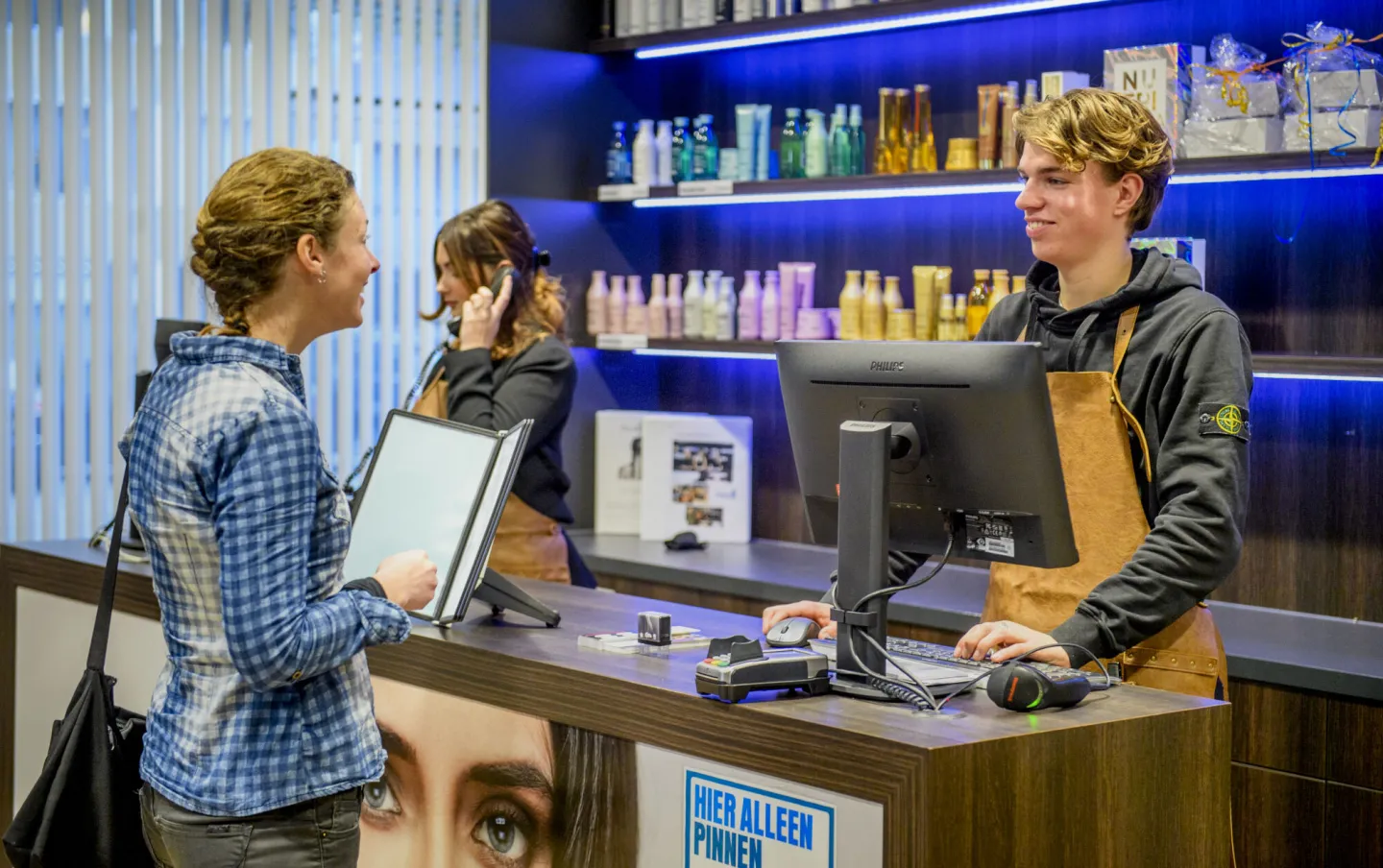 Een man en vrouw staan aan de toonbank in een kapperszaak.