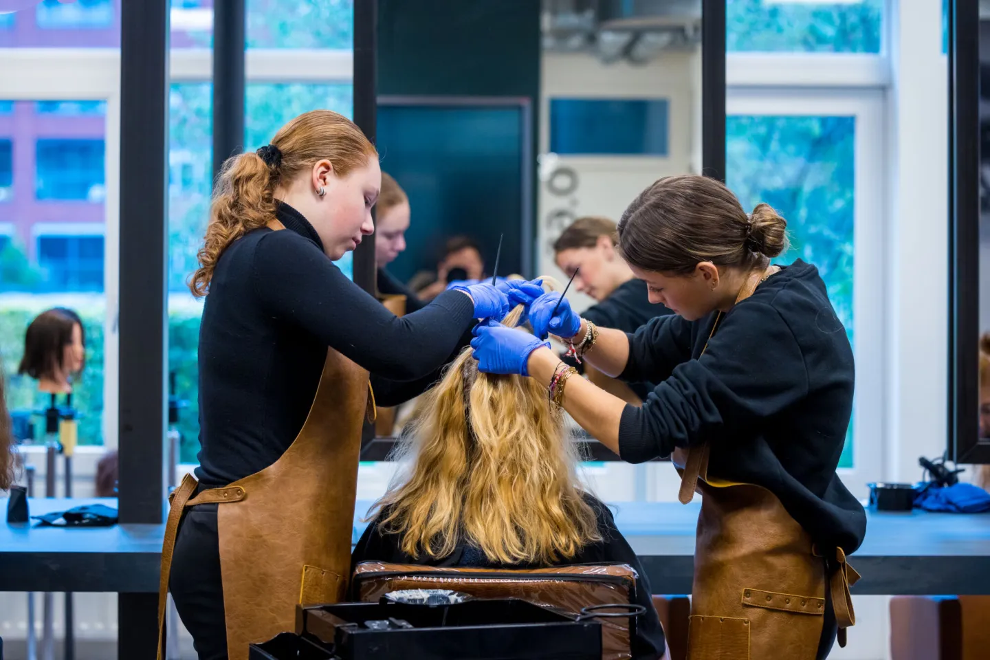 Twee dames stylen het haar van een vrouw in een kapsalon.