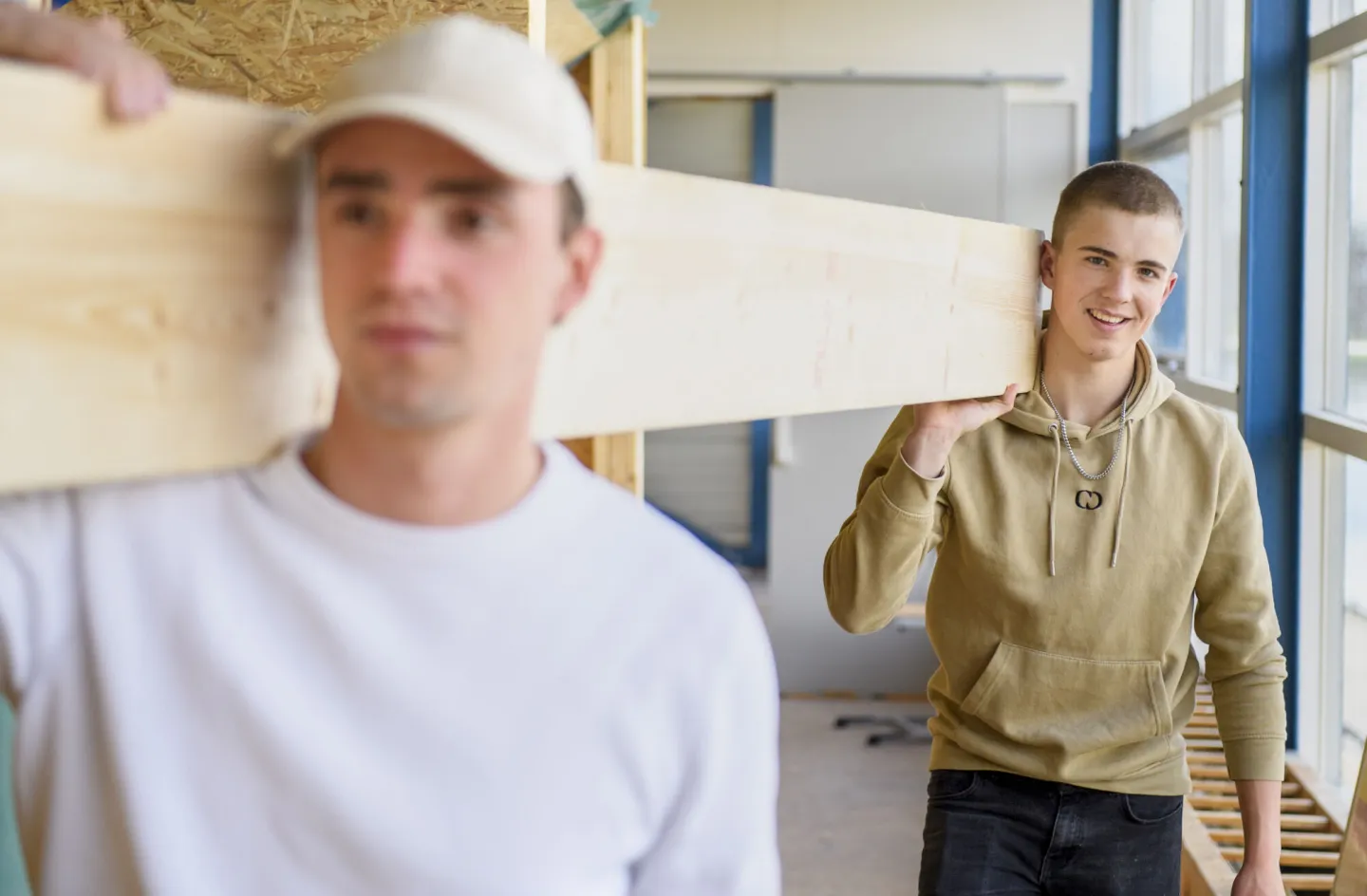 Twee studenten dragen samen het hout naar de werkbank.