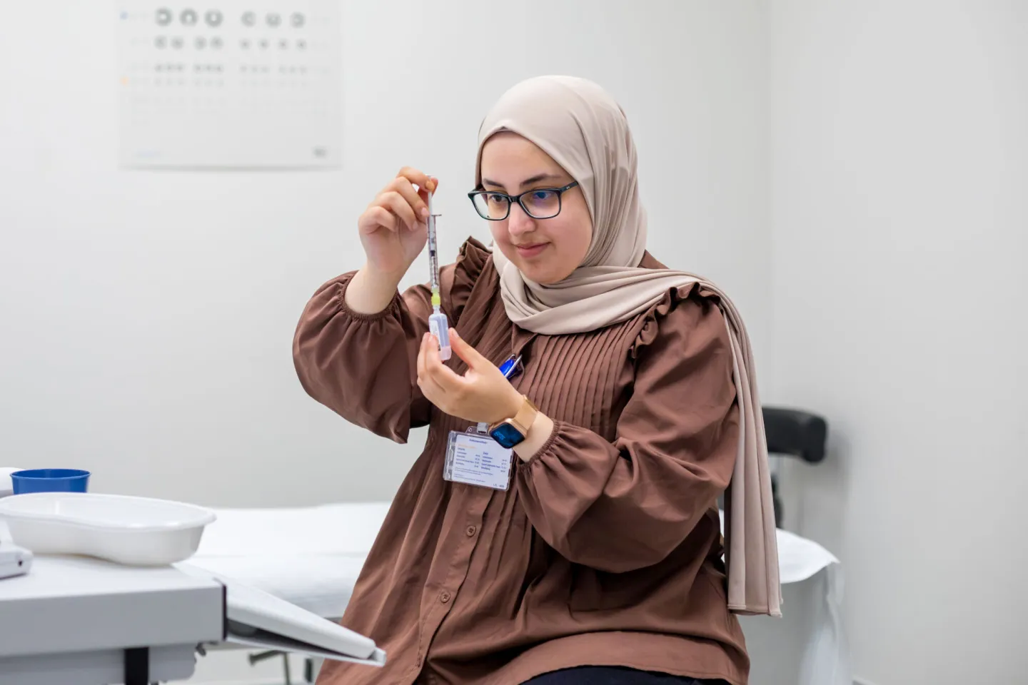 Een vrouw met een hijab zit aan een tafel met een injectienaald.