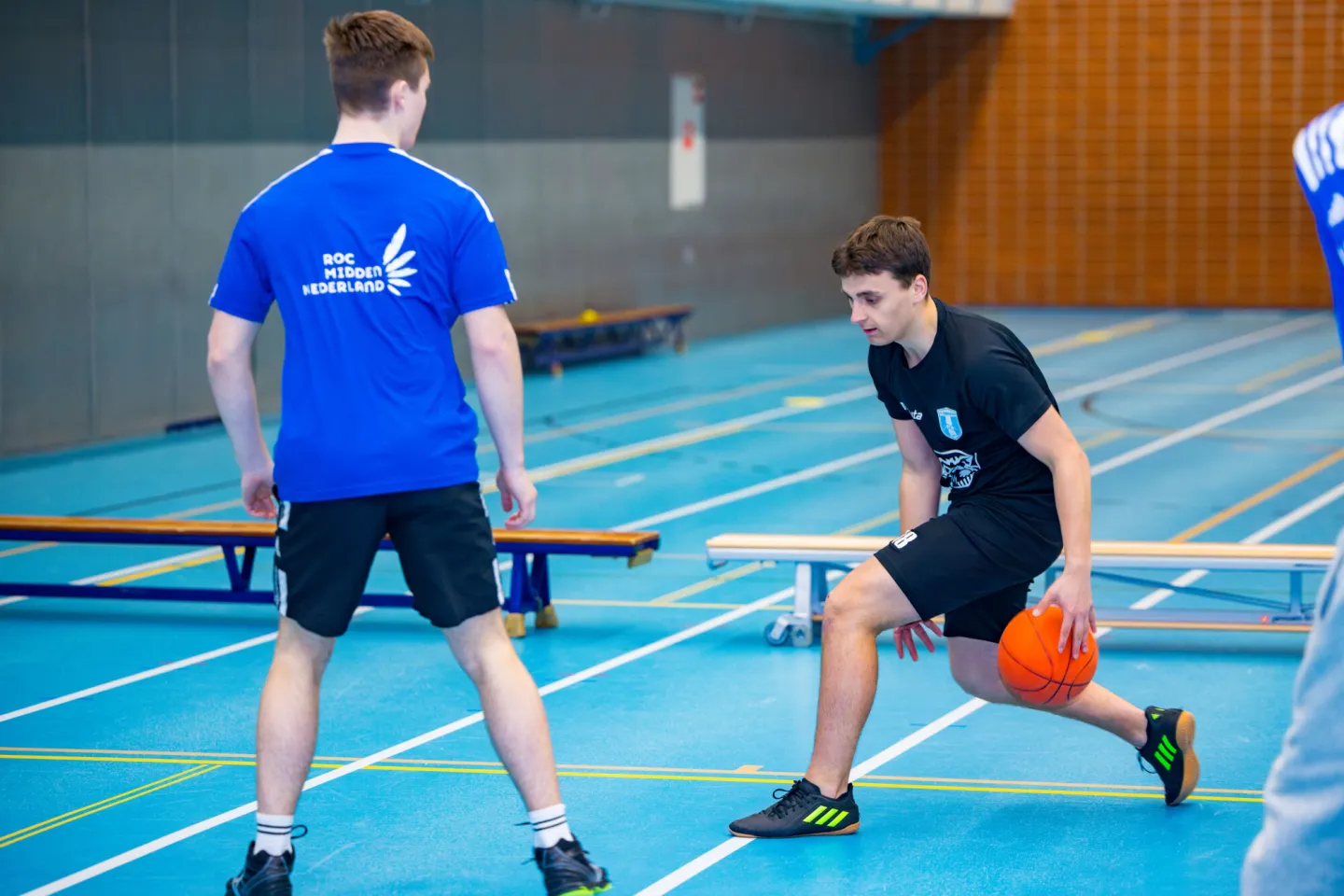 Twee jonge mannen spelen basketbal in een sporthal.