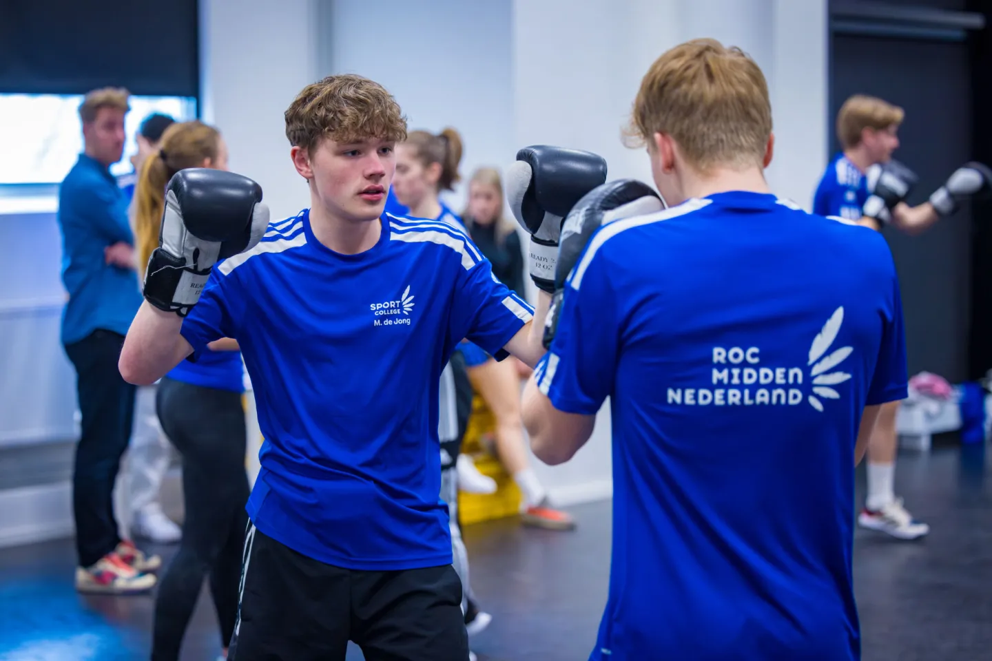 Twee jonge mannen in blauwe shirts en zwarte shorts oefenen boksen.