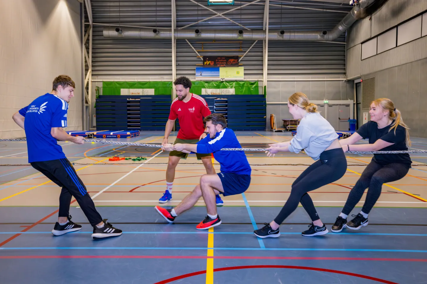 Een groep mensen speelt touwtrekken in een overdekte gymzaal.