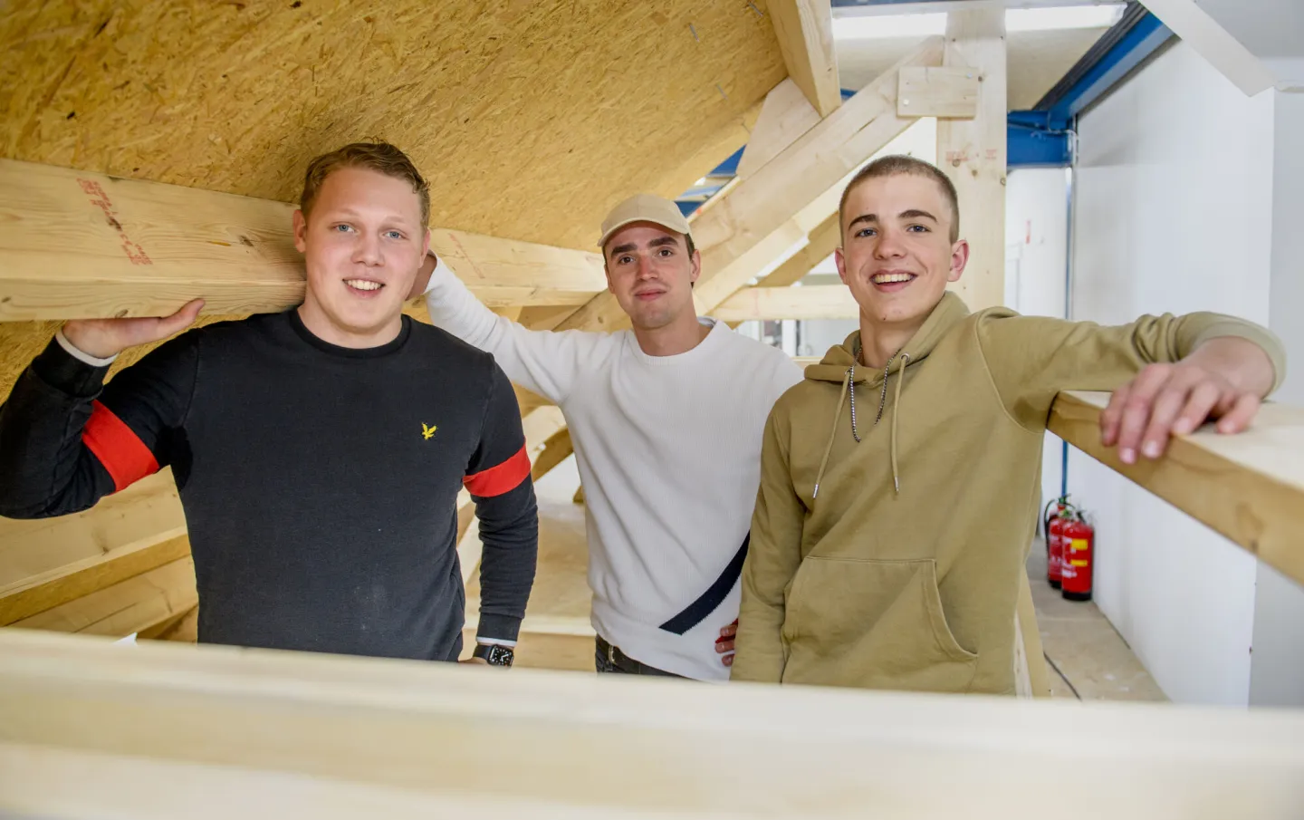 Drie studenten timmerman werken aan een kamer met houten balken. 