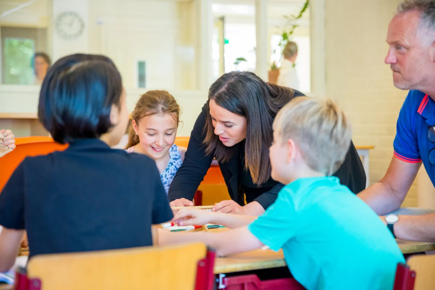 Groep kinderen en leraar aan tafel in klaslokaal. 