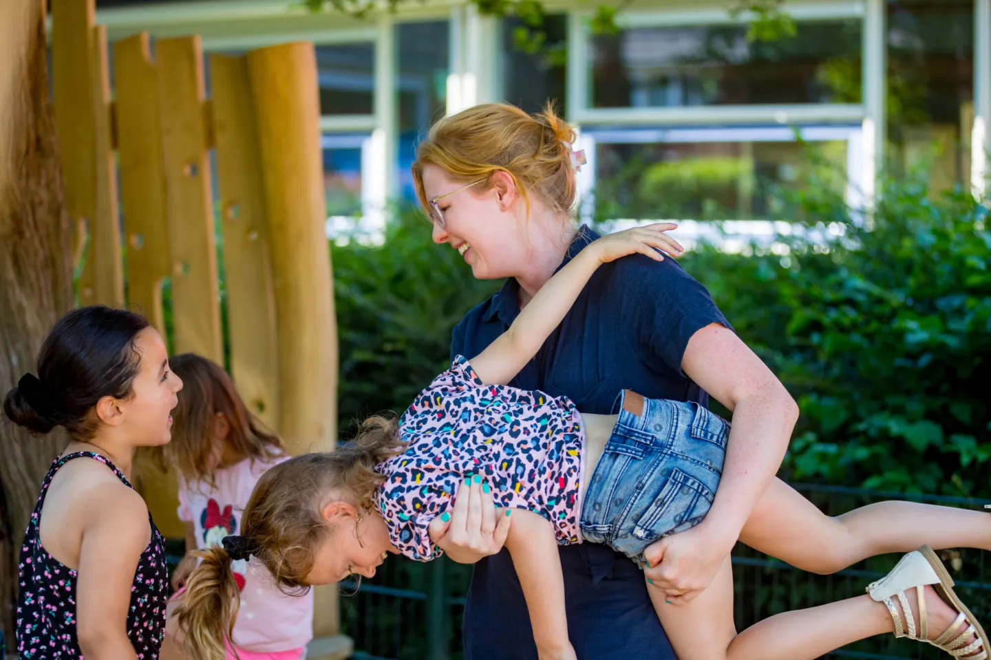 Een vrouw houdt een klein meisje in de lucht. Een vrolijke en speelse interactie tussen een begeleider en kinderen op een speelplaats