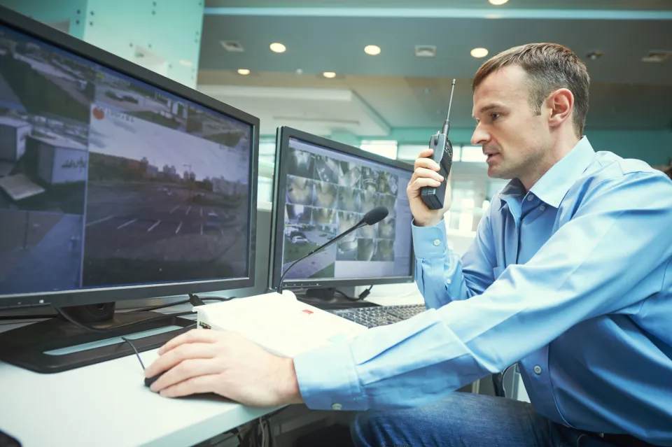 Beveiliger bekijkt beelden van bewakingscamera’s en praat in walkie talkie.