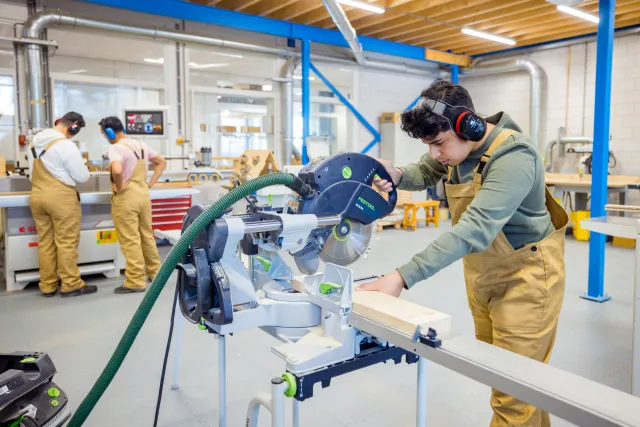 Student assistent bouw hout wonen werkt met zaagmachine in praktijklokaal