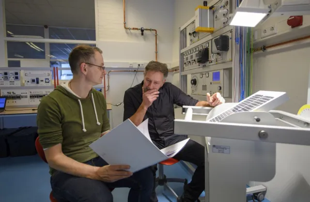 Een student Operator C warmte en energie in de praktijk met praktijkbegeleider voor een controlepaneel in de fabriek. 