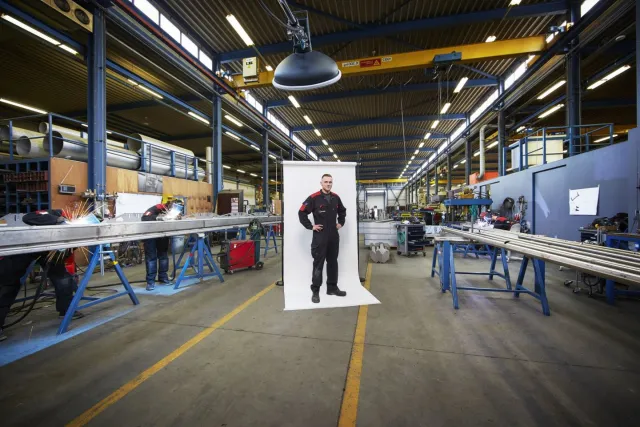 Student poseert op de werkplaats terwijl andere studenten aan het werk zijn 