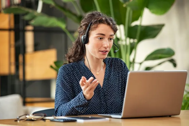 Volwassen vrouw achter de computer met headset als medewerker service desk. 