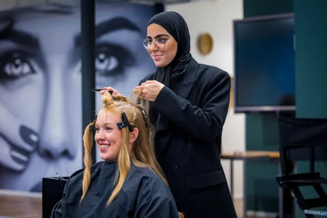 Een vrouw in een hijab knipt het haar van een andere vrouw.