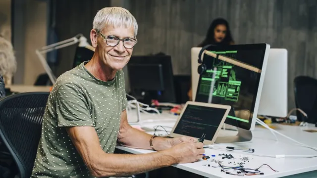 Cursist ICT techniek kijkt in de cameralens. Op de achtergrond computers, kabels zichtbaar. 