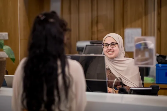 Doktersassistent in gesprek met patiënt aan balie. 