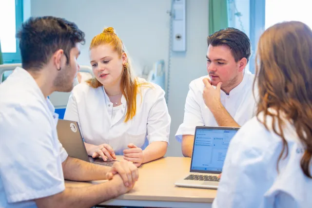 Personen in witte verpleegkundejassen zitten bijeen aan tafel.