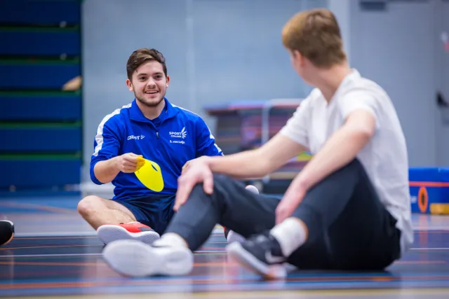 Man zit op de grond met een sportvoorwerp in zijn hand.