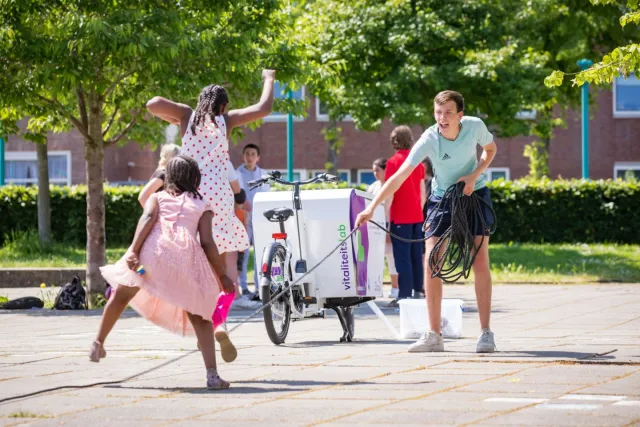 Twee meisjes aan het touwtje springen onder begeleiding van een pedagogisch medewerker. 