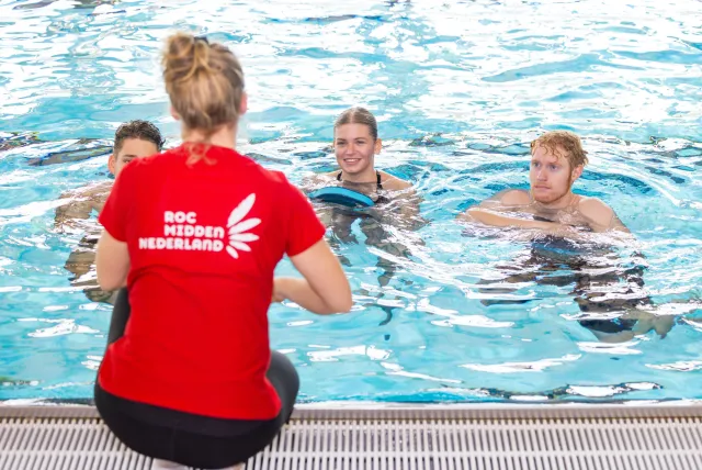 Zwemlessen in het zwembad: jonge mensen leren zwemmen onder begeleiding van een sportinstructeur.