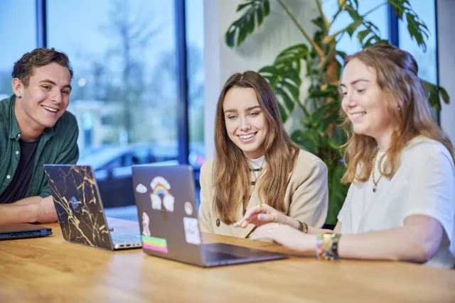 studenten zitten in kantine en bekijken iets op een laptop