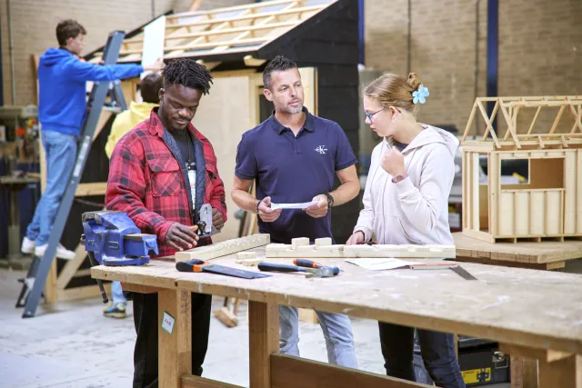 Studenten van de opleiding meubelmaker werken samen in de werkplaats met een docent 