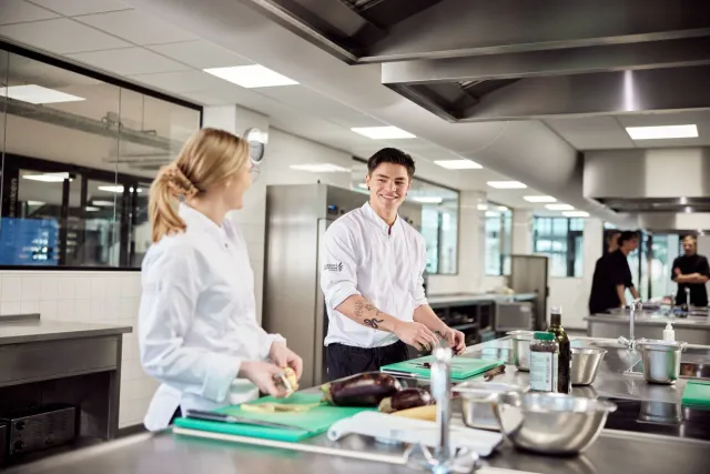 Studenten Zelfstandig Werkend Kok snijden groente in moderne keuken op school 