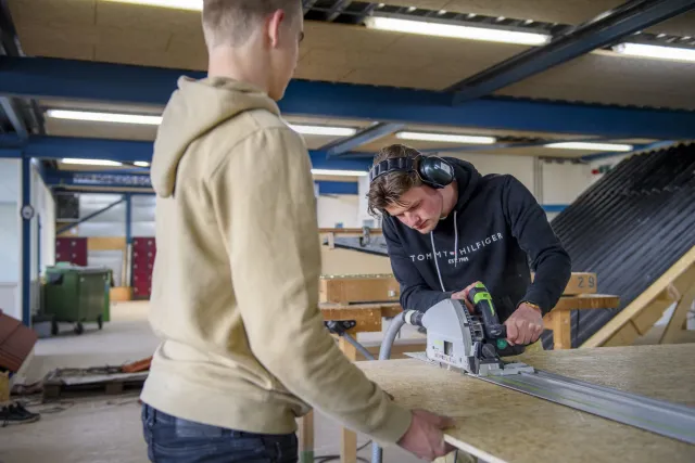 Studenten werken samen met een machine aan een object van hout 