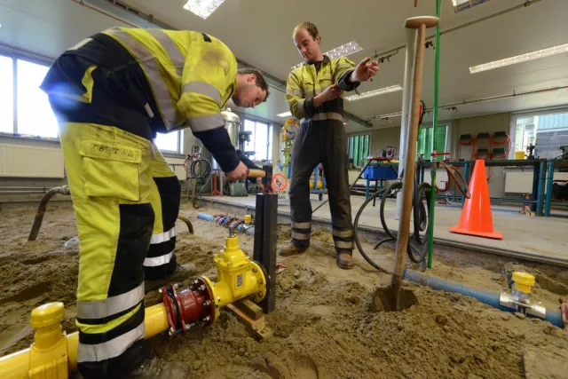 Twee monteurs gas-, water- en warmtedistributie werken aan een leiding op een bouwplaats. 