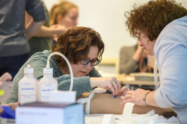 Verpleegkundige oefent met inbrengen infuus tijdens examentraining Verpleegkundige vaardigheden bij andere deelnemer. 