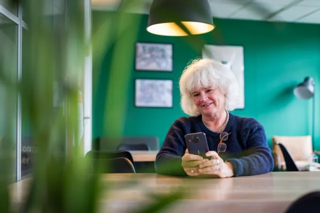 Vrouw zit in woonkamer en stuurt via mobiele telefoon gegevens door voor thuismonitoring. 