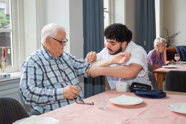 Student opleiding Verzorgende-IG controleert bloeddruk van oudere man. 