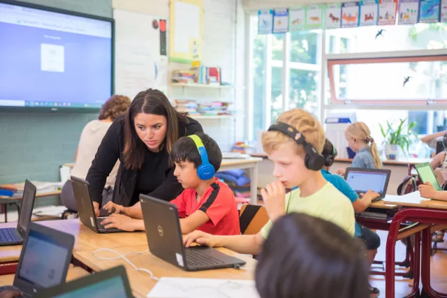 Klaslokaal met kinderen en laptops, leraar geeft les