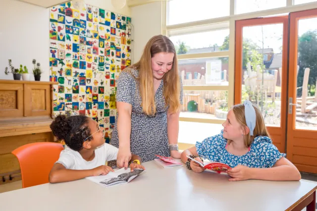 Een jonge vrouw en twee kinderen zitten aan tafel met boeken.