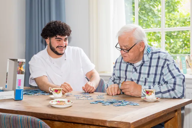 Een jonge man en een oudere man maken samen een legpuzzel. 