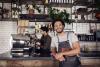 Barista in koffieshop leunt op de counter en achter hem maakt een collega koffie.