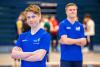 Twee jonge mannen in blauwe shirts staan in een sporthal.