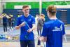 Twee jonge mannen in blauwe shirts staan in een sporthal.