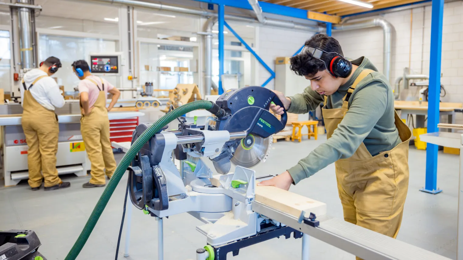 Student assistent bouw hout wonen werkt met zaagmachine in praktijklokaal