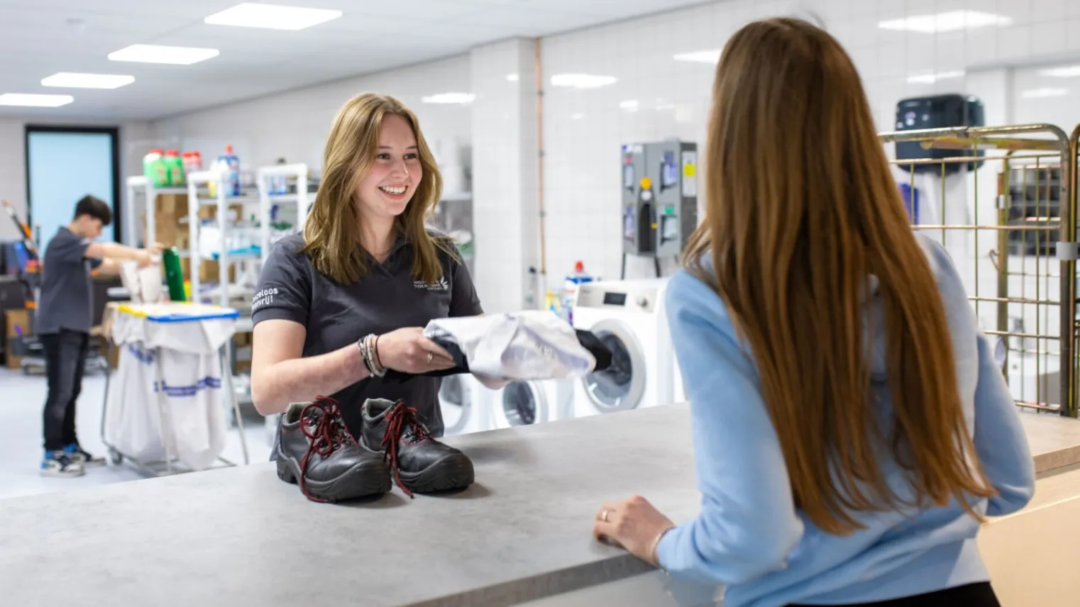 Student Assistent Dienstverlening geeft overhemd aan medewerker 