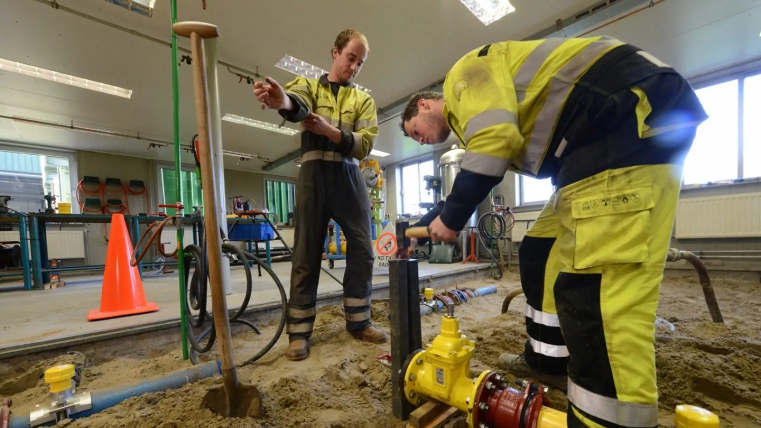 Twee monteurs gas-, water- en warmtedistributie werken aan een leiding op een bouwplaats. 