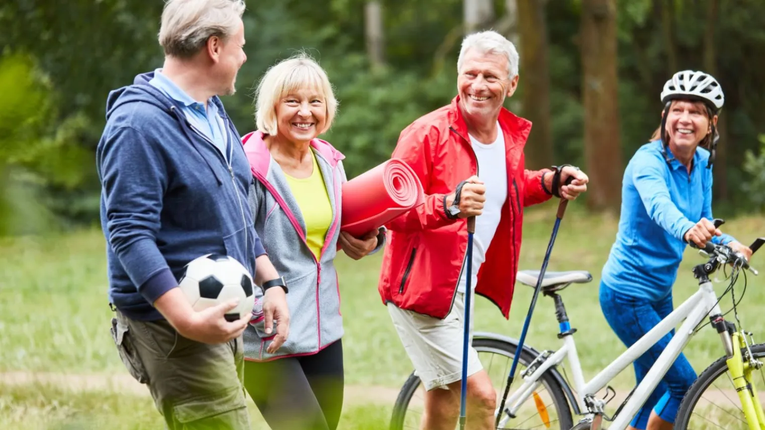 Vier volwassenen die sportief buiten zijn met voetbal, yogamat, Nordic walking sticks en een racefiets.