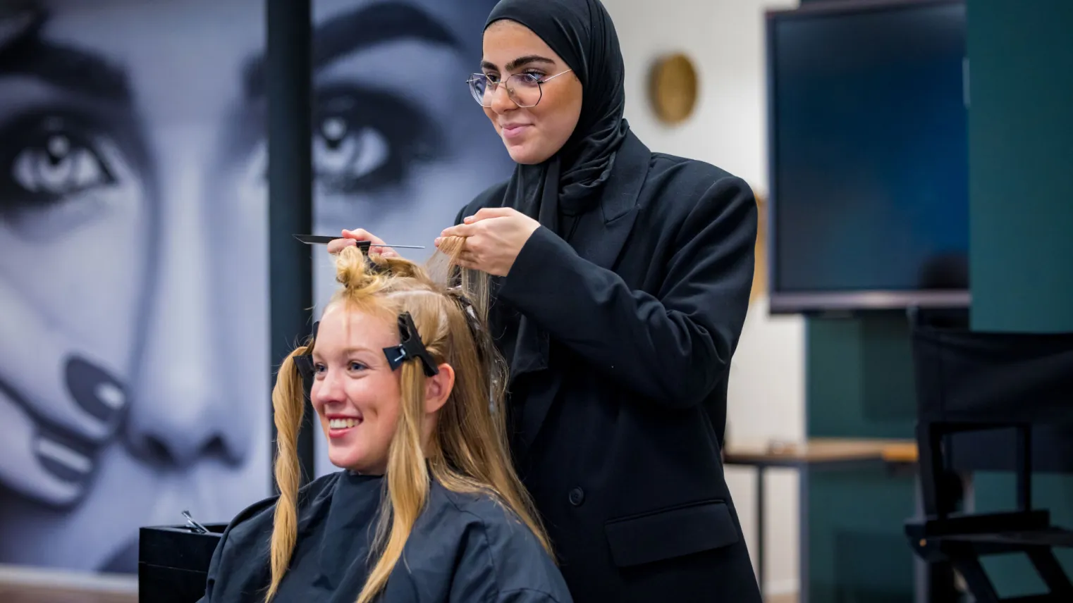 Een vrouw in een hijab knipt het haar van een andere vrouw.