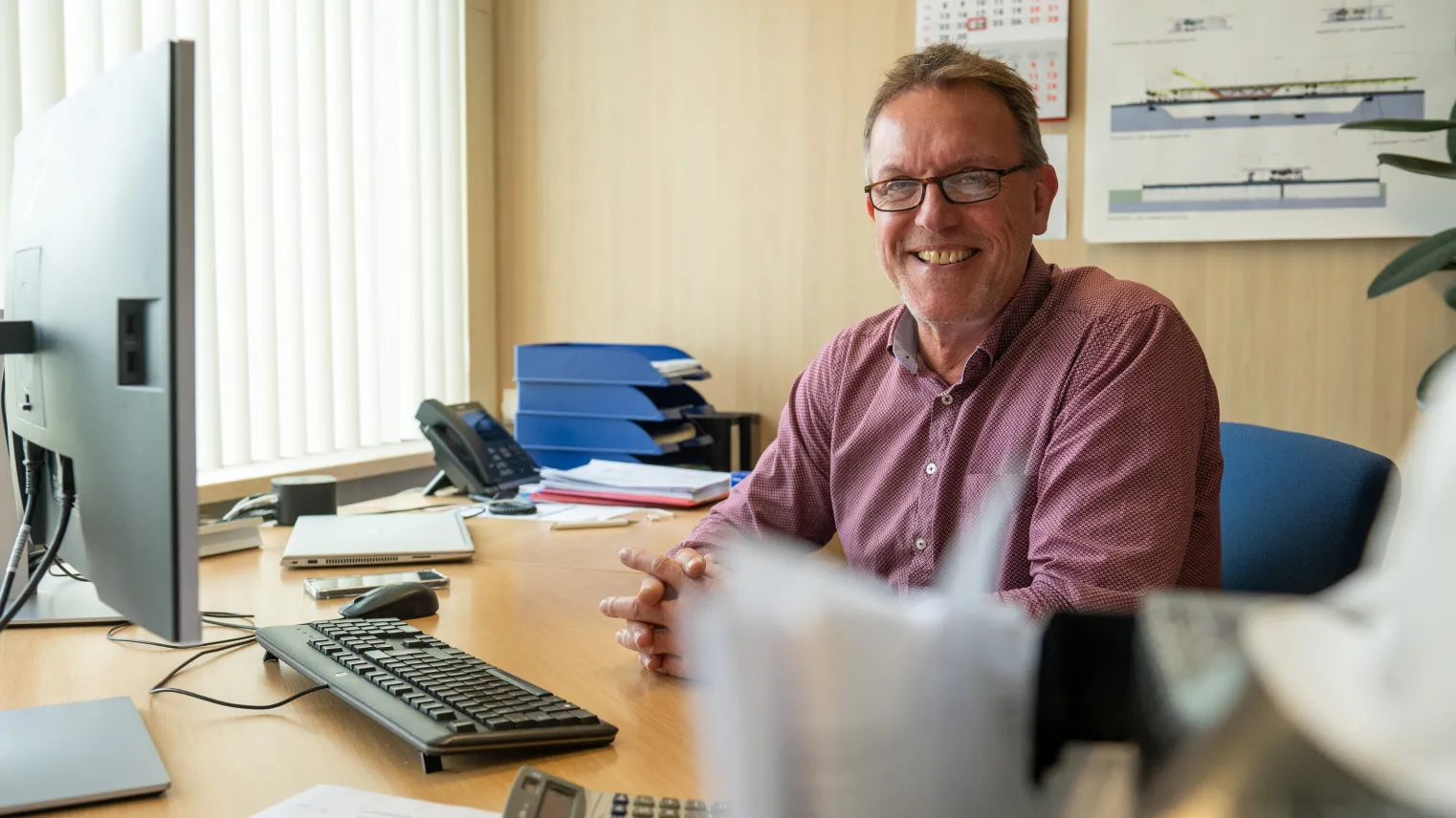 Commercieel medewerker zit aan bureau met computer en kijkt in camera.