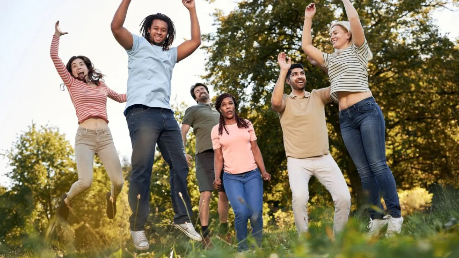 Groep mensen springt buiten met armen omhoog in de lucht.