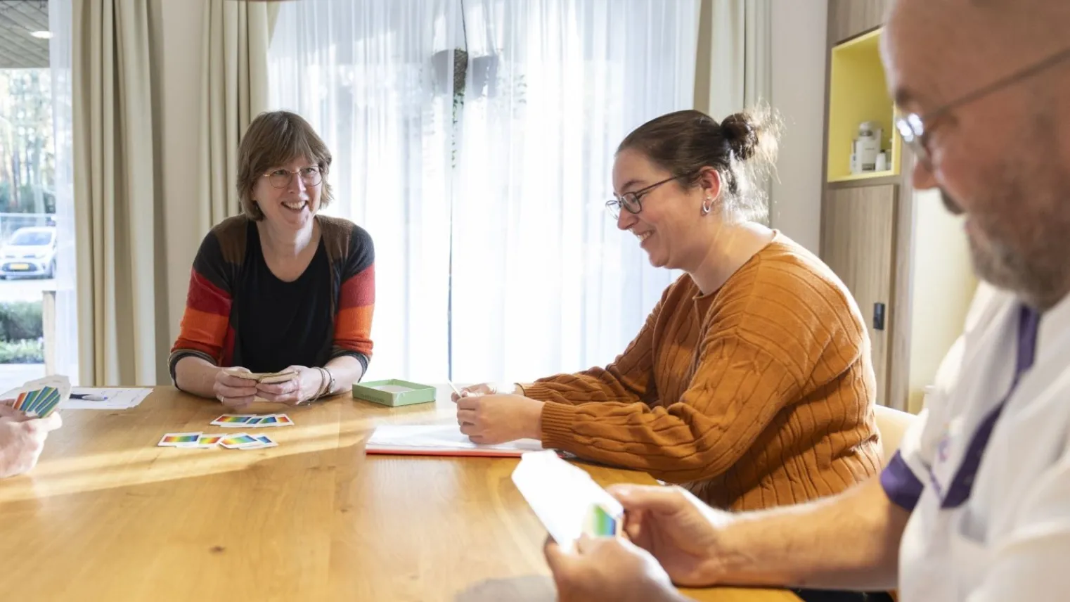 Praktijkopleider speelt aan tafel spel met coachkaarten met 2 werkbegeleiders. 