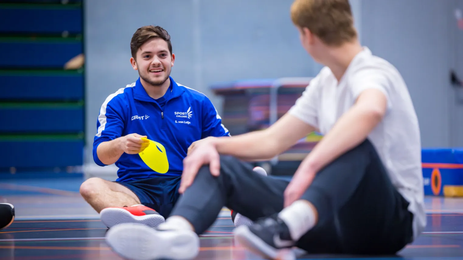 Man zit op de grond met een sportvoorwerp in zijn hand.