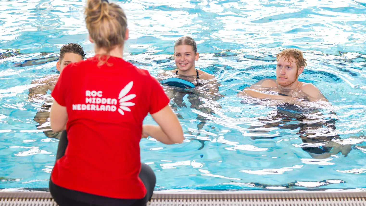 Zwemlessen in het zwembad: jonge mensen leren zwemmen onder begeleiding van een sportinstructeur.